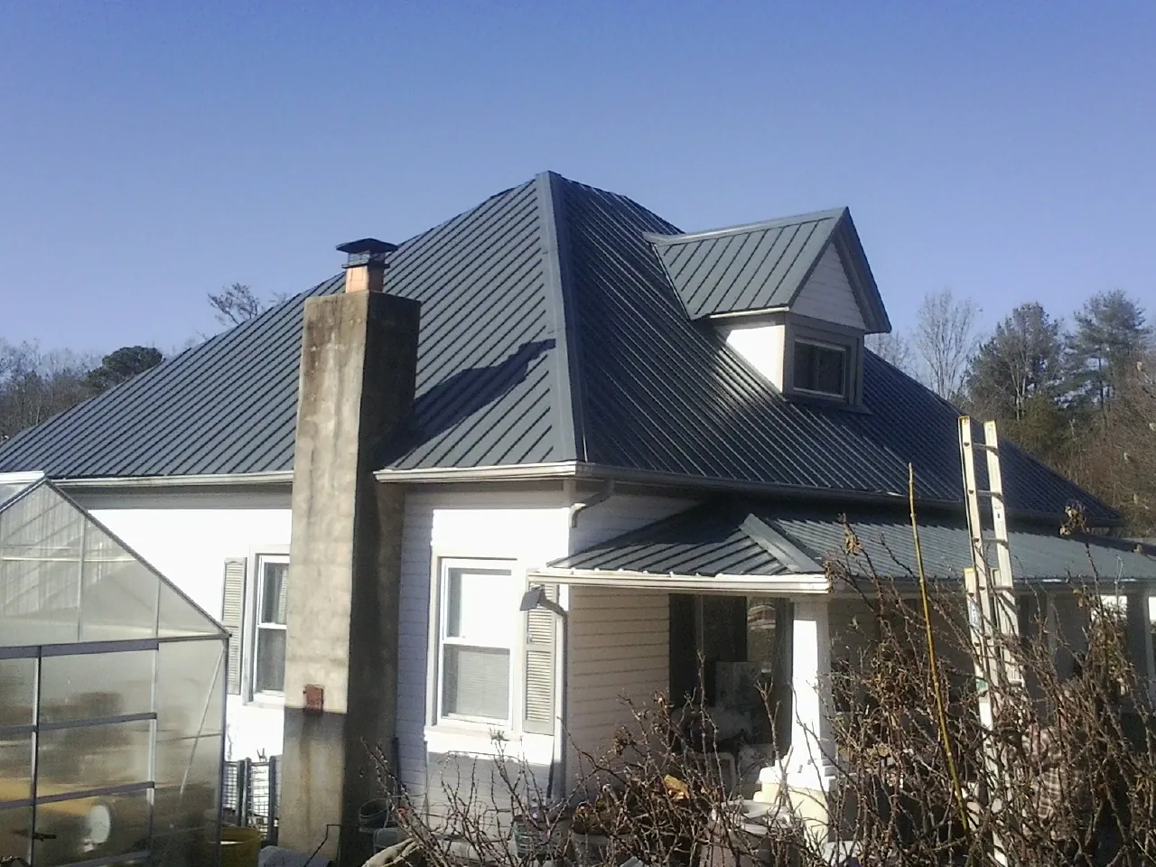 Dark blue standing seam metal roof on a white farmhouse with dormer — Slate & Tile Roof Repair by Roofing Brothers in Vernon