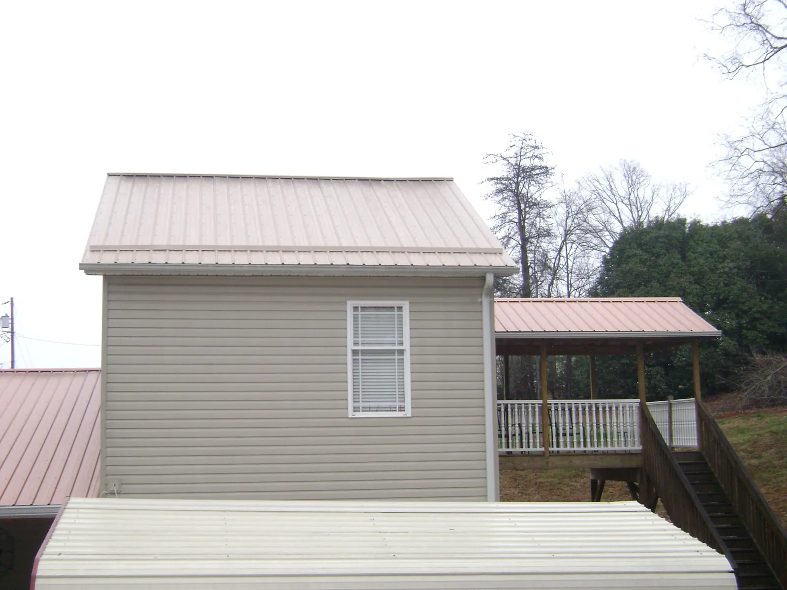 Tan metal roofs on a two story addition and attached porch, from a Roof Replacement job in Vernon